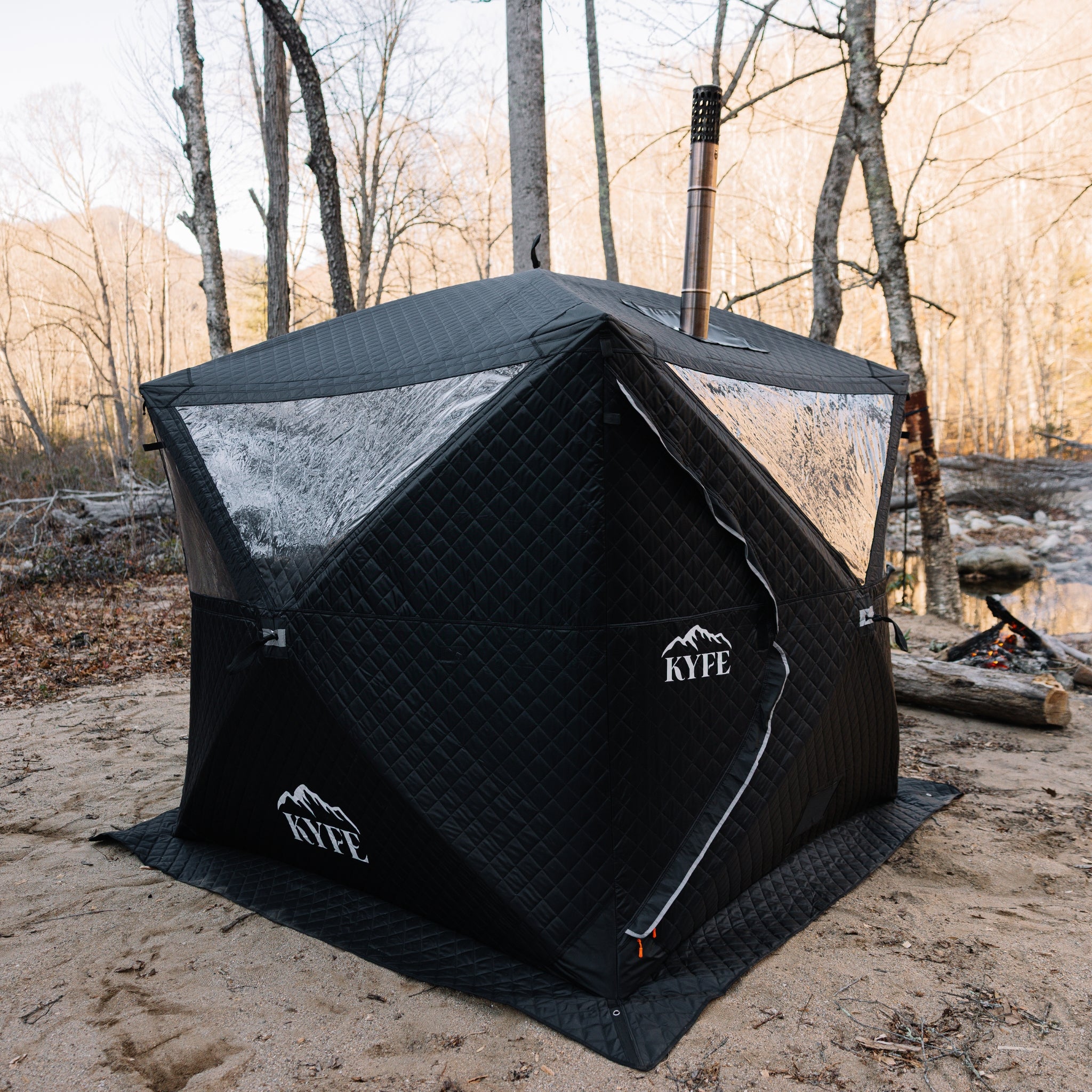 Black KYFE portable sauna tent set up on sand with forest background – wood-burning sauna tent