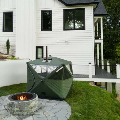 Forest green KYFE portable sauna tent set up in backyard next to stone fire pit – outdoor wood-fired sauna tent for home use