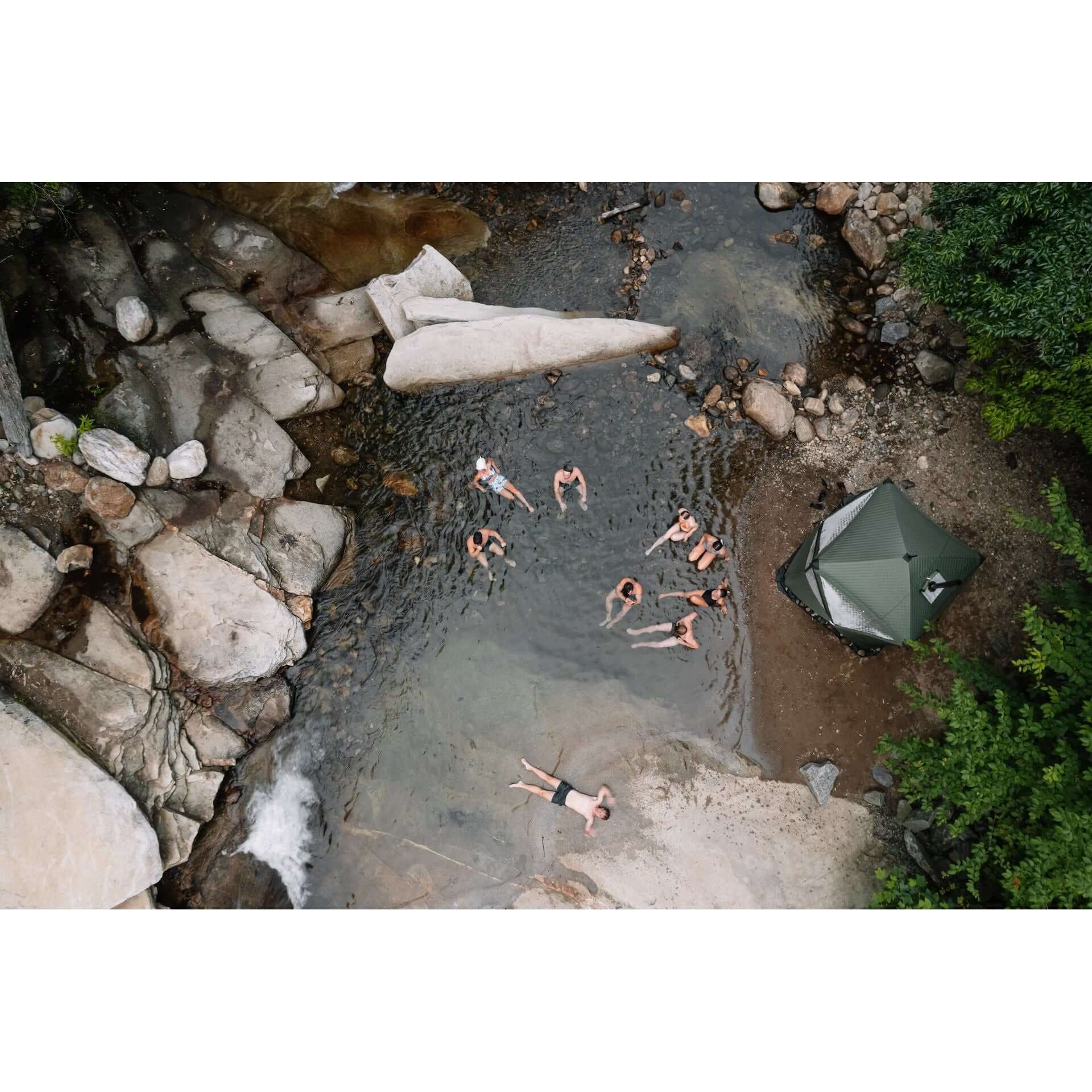 Aerial view of group cold plunging in natural river beside forest green KYFE portable sauna tent – outdoor sauna and cold plunge wellness experience